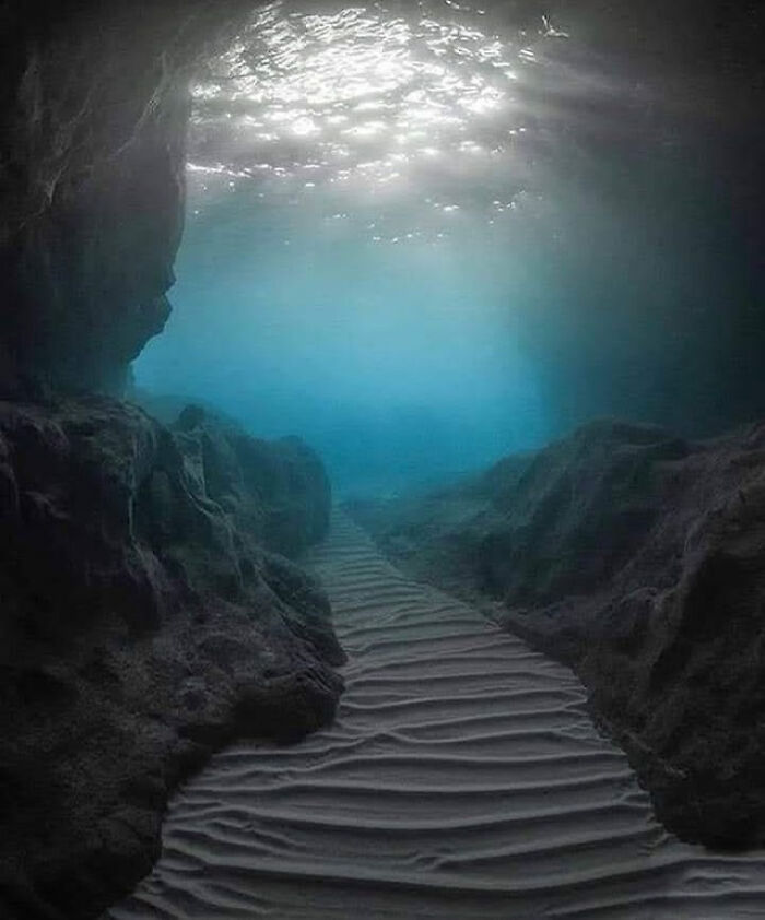 Underwater deep-water cave path with rocky walls and sunlight from above