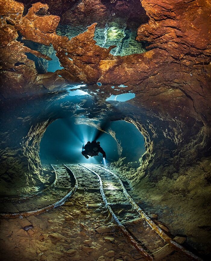 Diver exploring rusty underwater tunnel with old rail tracks and deep water surroundings