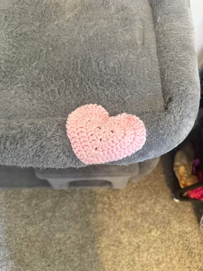 A small crocheted pink heart covering damage on a grey cat tree, demonstrating how creativity can save money.