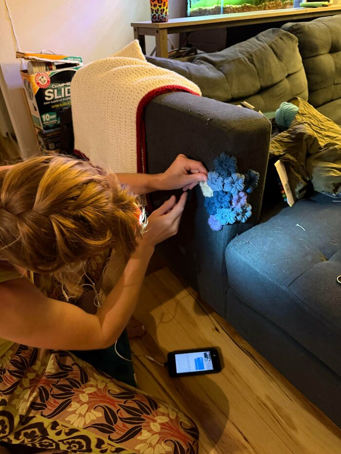 A person using creativity to mend a couch arm with crocheted flowers, showing how to save money.