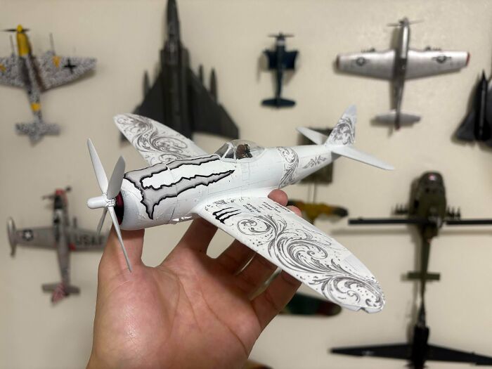 Hand holding miniature model of decorative white airplane with aircraft background