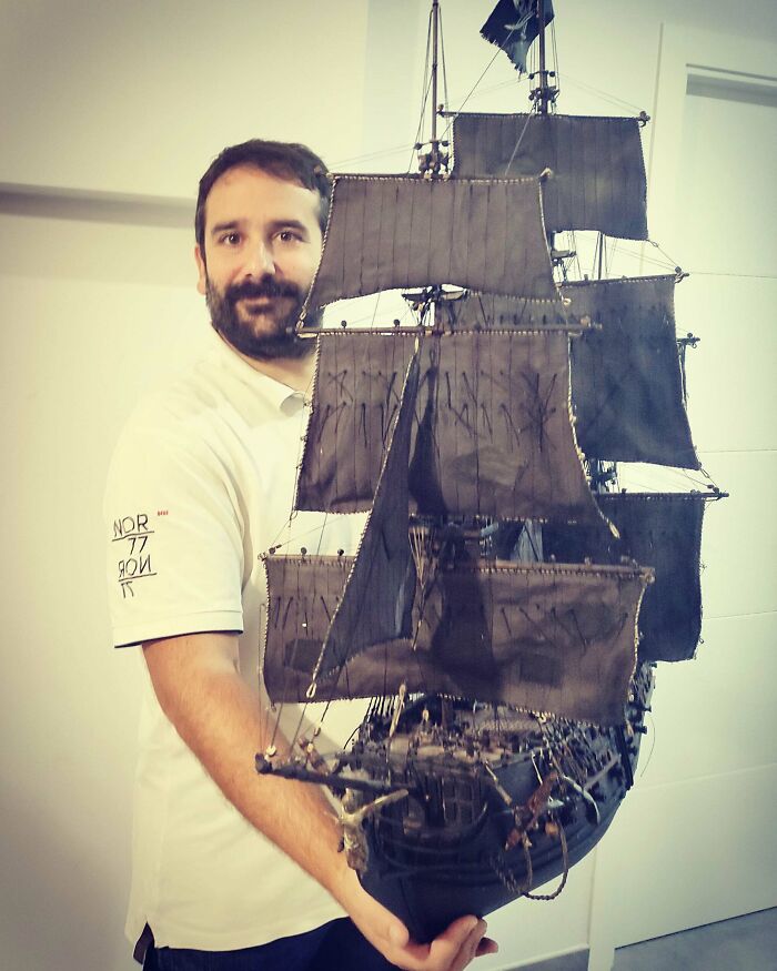 Man holding a large, detailed miniature model of a ship with black sails