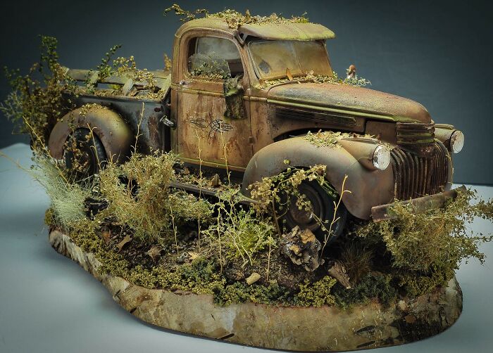 Weathered miniature old pickup truck covered with moss and plants on natural base