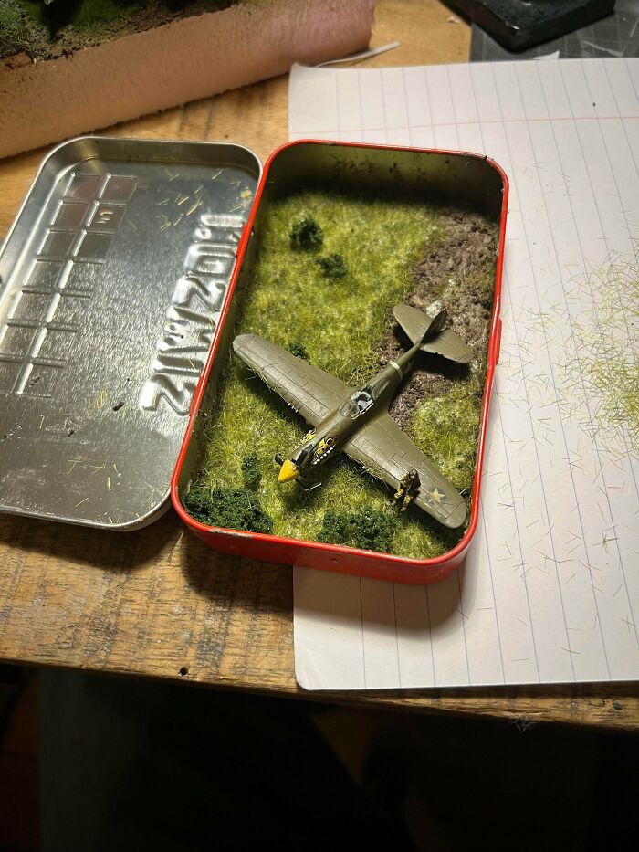 Miniature WWII airplane displayed in a small grass-covered box