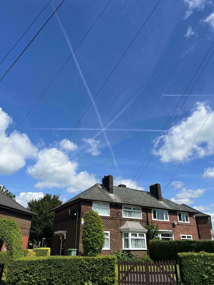 Contrail lines in the sky forming an X above suburban houses