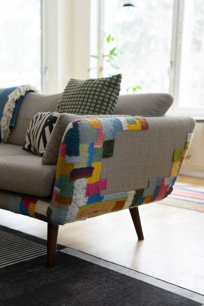 A grey couch showcasing creativity by using colorful woven patches to repair worn armrests and save money.