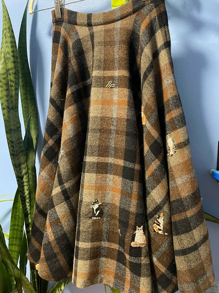 Plaid woolen skirt with small embroidered cats covering moth holes, proving creativity can save money.