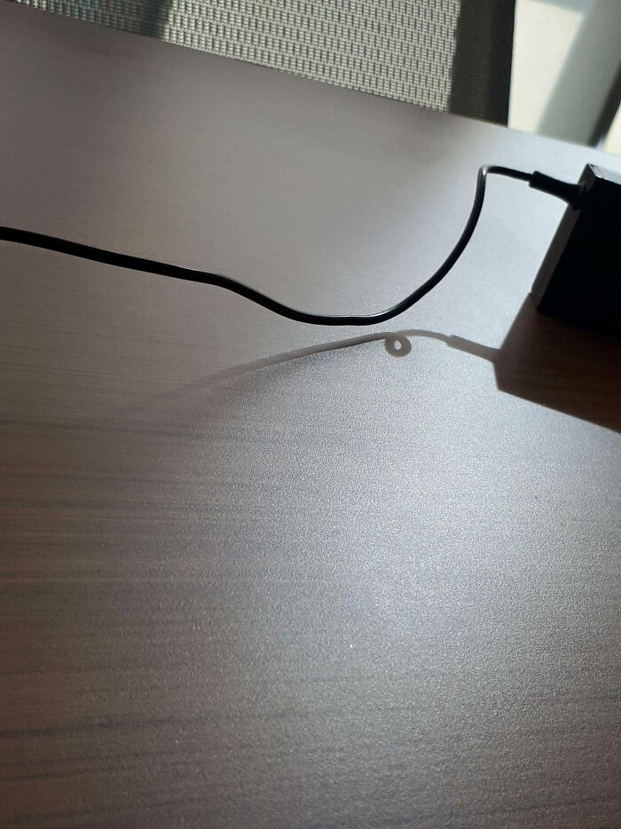 Shadow of a charging cable forming a loop on a table mimicking a digital glitch effect
