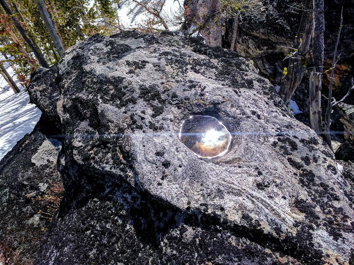 Sunlight reflecting from a water droplet on a dark rock surface