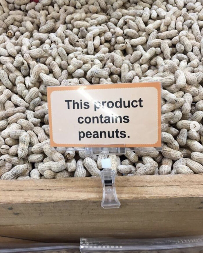 A sign placed in a bin of whole peanuts reading 'This product contains peanuts' as an example of confusing labels.