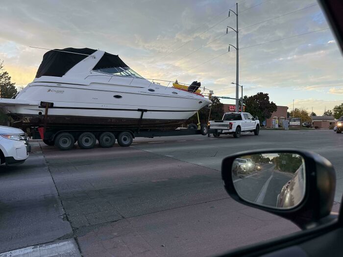Massive white boat being towed on a multi-axle trailer across a city street, an example of risky towing gone wrong.