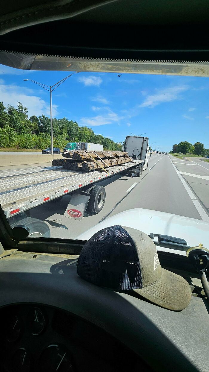 Flatbed semi truck carrying unsecured metal pipes on the highway, demonstrating towing gone wrong.