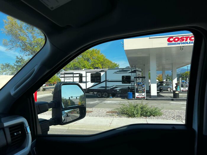 View from inside a vehicle showing a large RV camper being pulled past a gas station pump, an example of towing gone wrong.