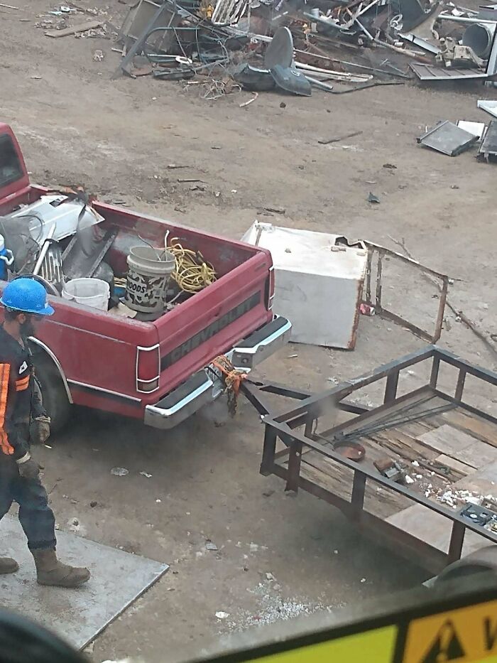 A red pickup truck in a scrapyard showcasing an example of towing gone wrong with a tied-on trailer hitch.