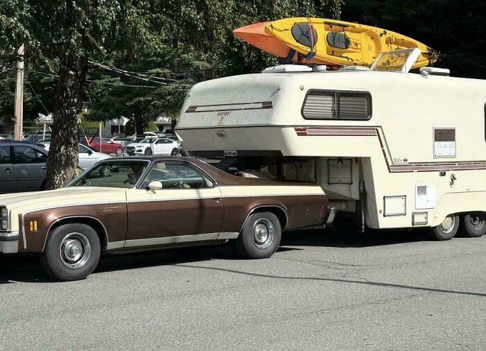 A brown car towing a large camper trailer with kayaks on top showing an unsafe towing gone wrong setup.