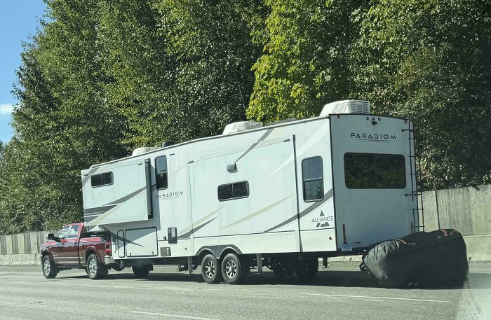 A red pickup truck hauling a massive fifth-wheel RV trailer showing a dangerous towing gone wrong situation.