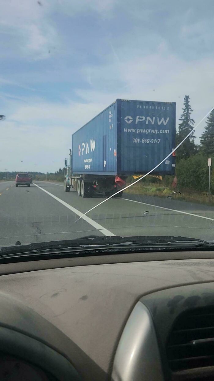 A semi-truck carrying a massive shipping container that severely overhangs the trailer bed, showing towing gone wrong.