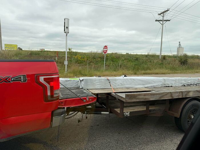 Red pickup truck pulling a flatbed trailer dangerously attached, a case of towing gone wrong.