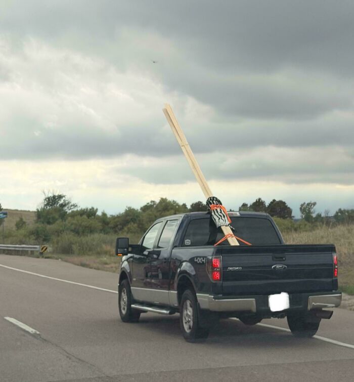 A dark pickup truck transporting excessively long wooden planks tied loosely, a classic case of towing gone wrong.