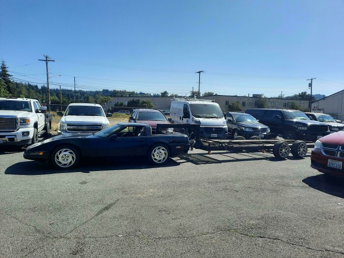 Black sports car towing an oversized flatbed trailer parked in a lot, showing towing gone wrong