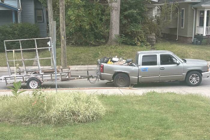 A silver pickup truck towing a dangerously overloaded and tilted utility trailer with equipment.