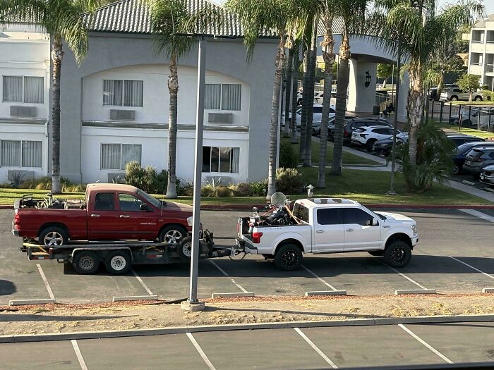 A white pickup truck towing a flatbed carrying another red truck, showing towing gone wrong.