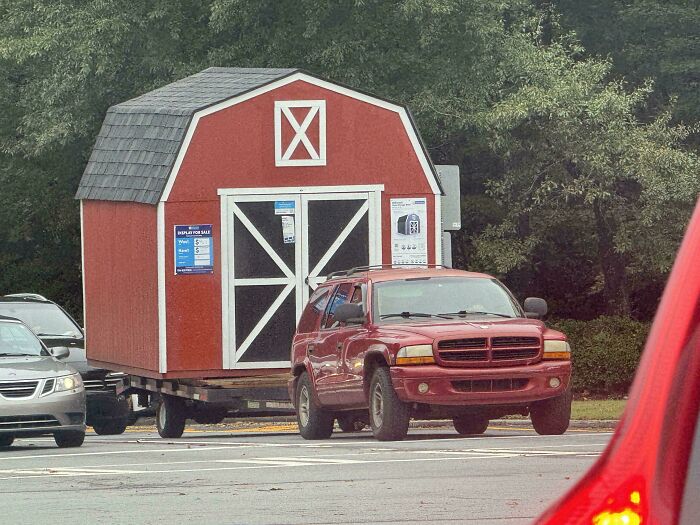 A red SUV towing a large wooden shed on a trailer in an example of towing gone wrong.