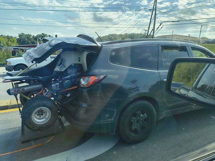 SUV driving with an ATV crammed inside the rear trunk with the hatch wide open, an example of towing gone wrong.