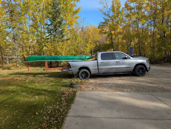 Silver pickup truck carrying a green canoe extended far out on a wooden rack, an example of towing gone wrong.