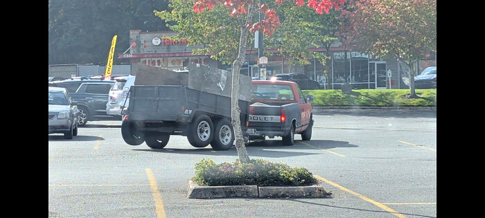 A pickup truck hauling a heavily tilted trailer, an example of towing gone wrong in a parking lot.