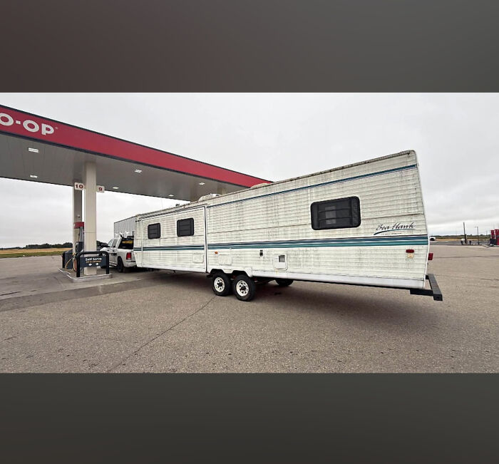 A pickup truck towing an excessively long white camper trailer at a gas station, demonstrating towing gone wrong.