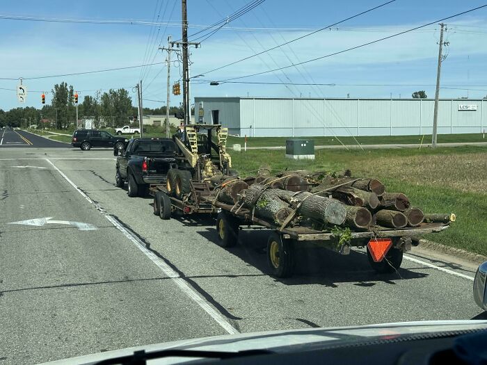 A pickup truck towing multiple heavily overloaded trailers filled with logs, an example of towing gone wrong.