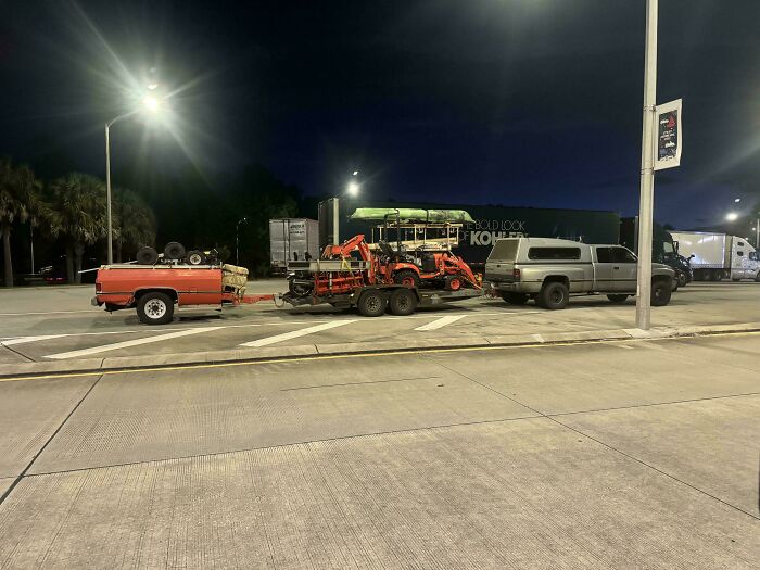 Silver truck towing an overloaded double trailer with machinery and a pickup bed attached, showcasing towing gone wrong.
