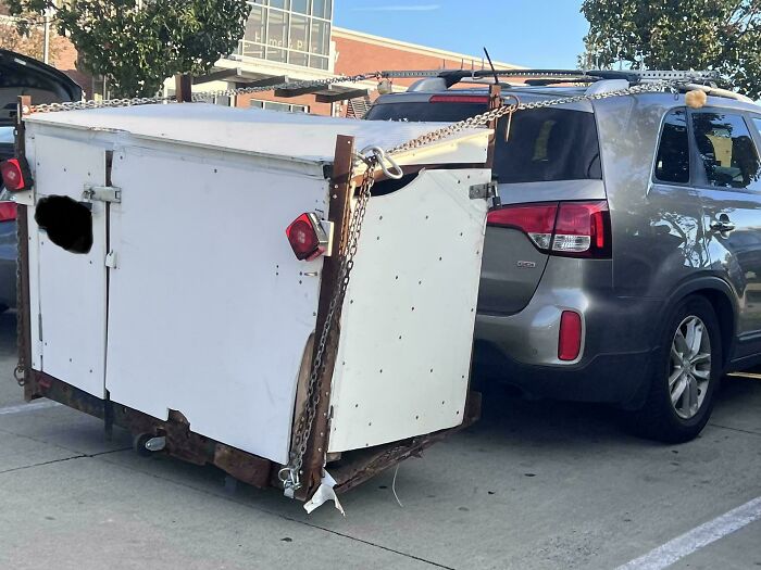 SUV attempting to tow a makeshift homemade wooden box trailer on small wheels, an example of towing gone wrong.