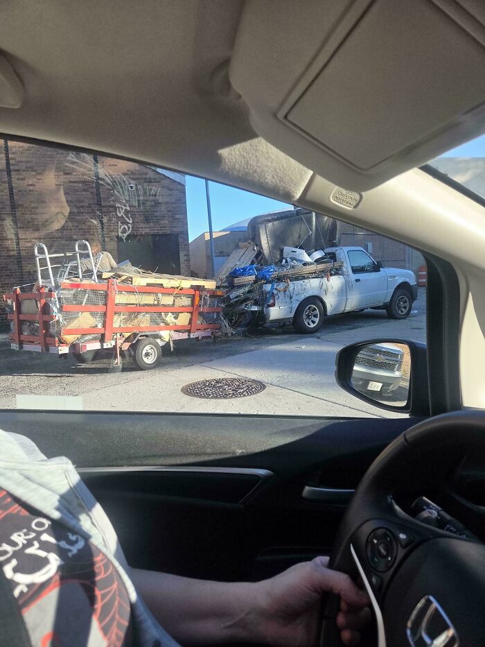 A white pickup truck dangerously overloaded with junk pulling a trailer in an example of towing gone wrong.