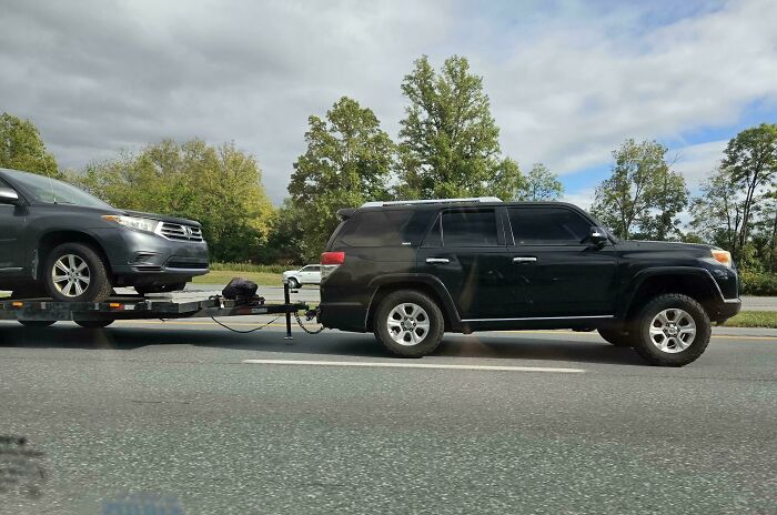 An SUV towing another vehicle on a trailer, showing a risky towing setup.