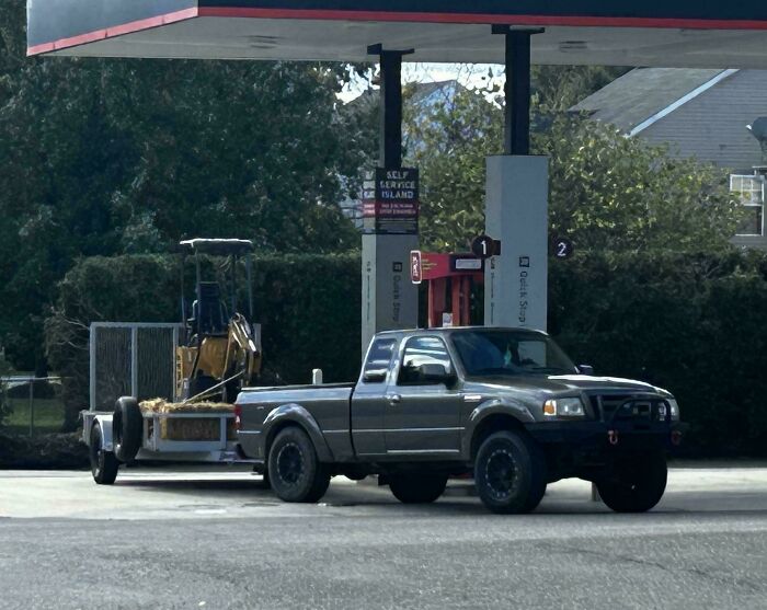A small pickup truck pulling an oversized construction digger, showing towing gone wrong.