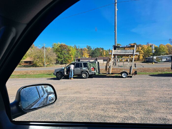 An SUV towing a homemade wooden structure on a small trailer along the road.