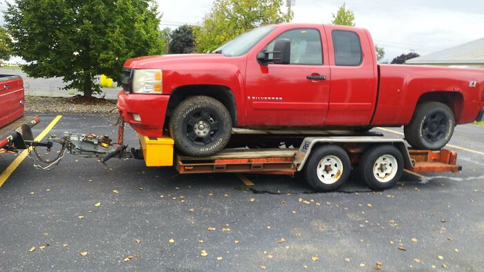 A large red truck loaded onto a small trailer, showcasing towing gone wrong
