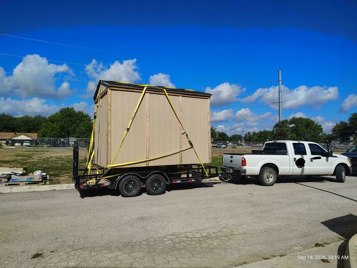 A white pickup truck transporting a large wooden shed on a trailer, demonstrating towing gone wrong
