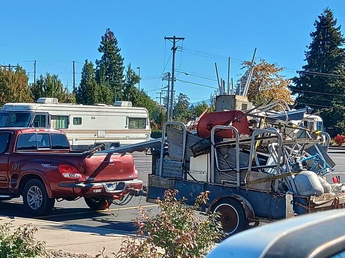 A red pickup truck towing a trailer excessively overloaded with scrap metal, demonstrating towing gone wrong.
