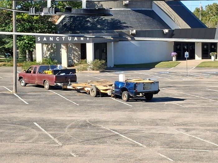 A red pickup truck towing an improvised flatbed trailer in a parking lot, showing towing gone wrong