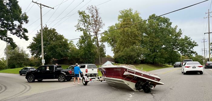 A motorboat fallen off its trailer and lying sideways on the road, showing an example of towing gone wrong.