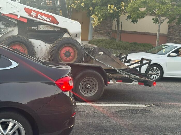 A Bobcat skid steer loader secured awkwardly on a flatbed trailer, illustrating towing gone wrong.