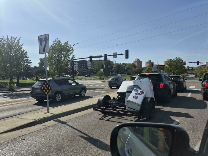 An open trailer carrying unsecured appliances sitting in traffic, an example of towing gone wrong.