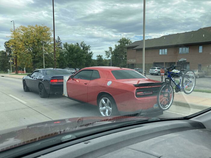 A red Dodge Challenger attached to a dark car showing towing gone wrong on the street