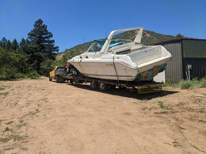 Large white boat towed on flatbed trailer, example of towing gone wrong on dirt road.