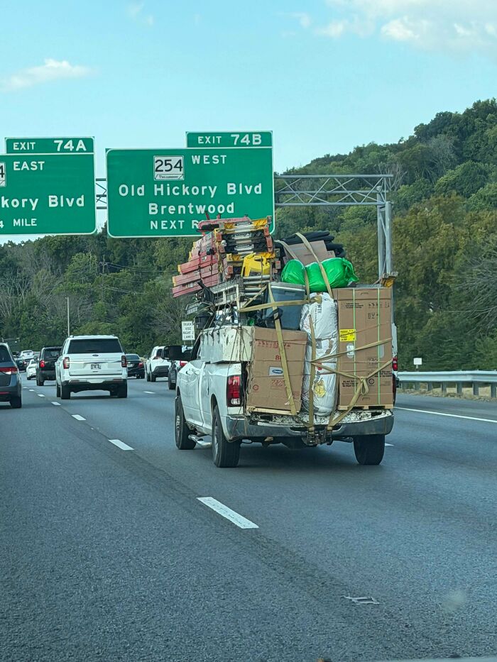 Overloaded white pickup truck driving on highway with stacked boxes, an example of towing gone wrong.