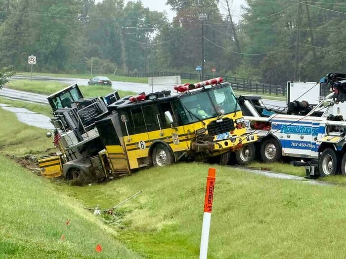 A yellow fire truck stuck in a ditch being pulled out by a heavy tow truck after a towing fail