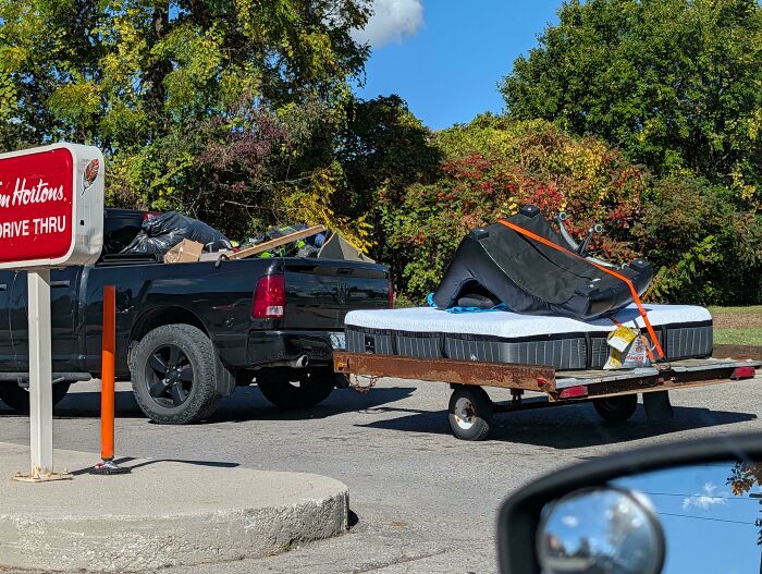 Pickup truck towing a mattress and office chair on a small trailer showing towing gone wrong